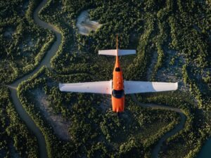 Top-down view of a Cirrus SR Series G7 aircraft flying above winding rivers and green landscape