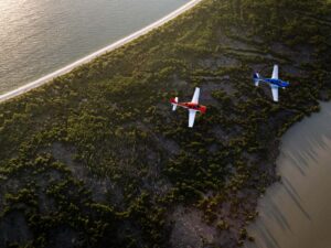 Two Cirrus SR Series G7 aircraft flying in formation along a forested coastline