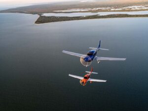 Two Cirrus SR Series G7 aircraft flying in formation over open water near the coastline