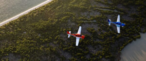 Two Cirrus SR Series G7 aircraft flying in formation along a forested coastline